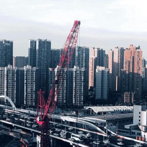 A cityscape with a red crane and bustling traffic below towering skyscrapers, showcasing urban development.