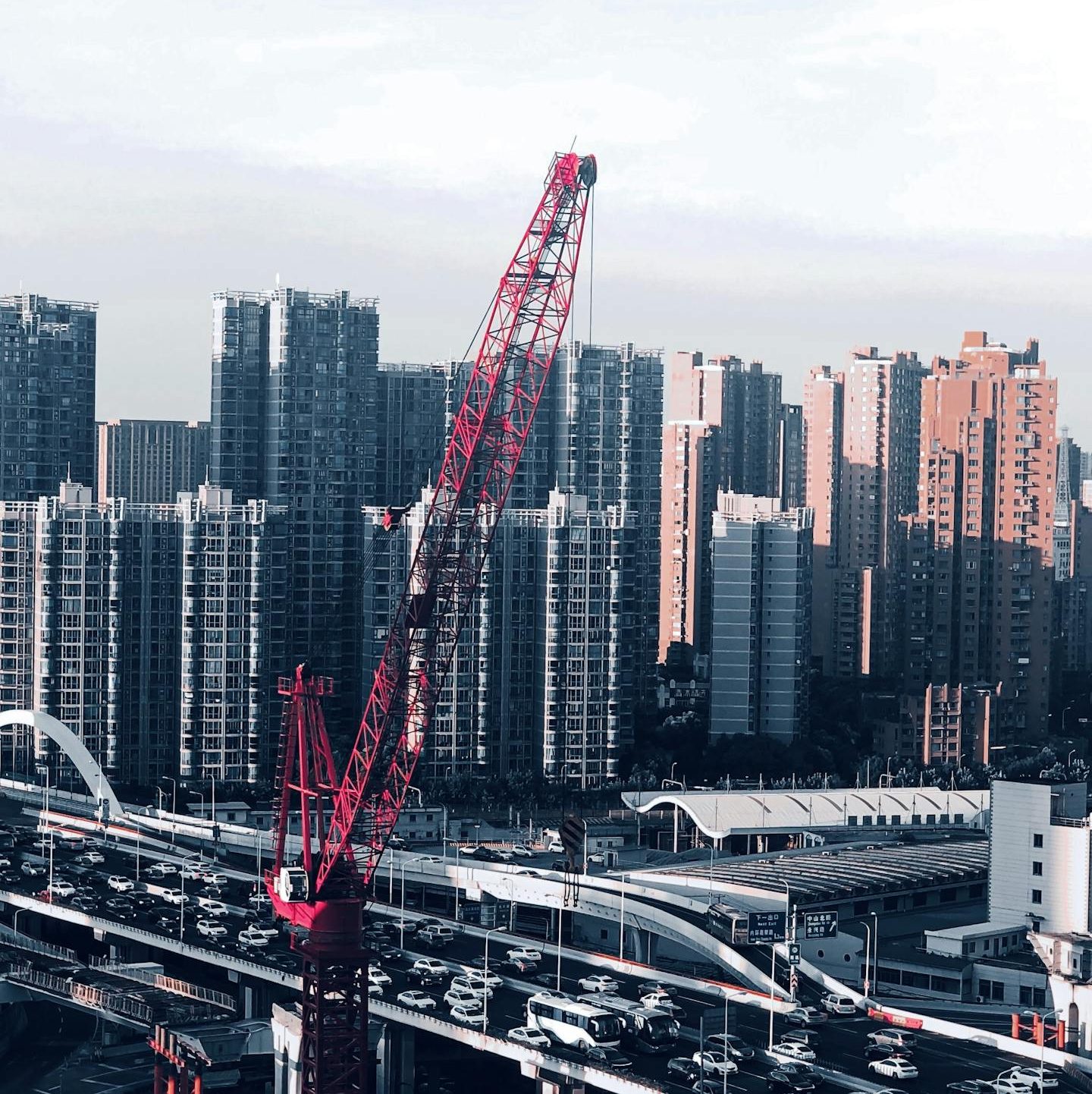 A cityscape with a red crane and bustling traffic below towering skyscrapers, showcasing urban development.