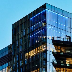 A sleek glass office building with illuminated interior visible against a twilight sky.
