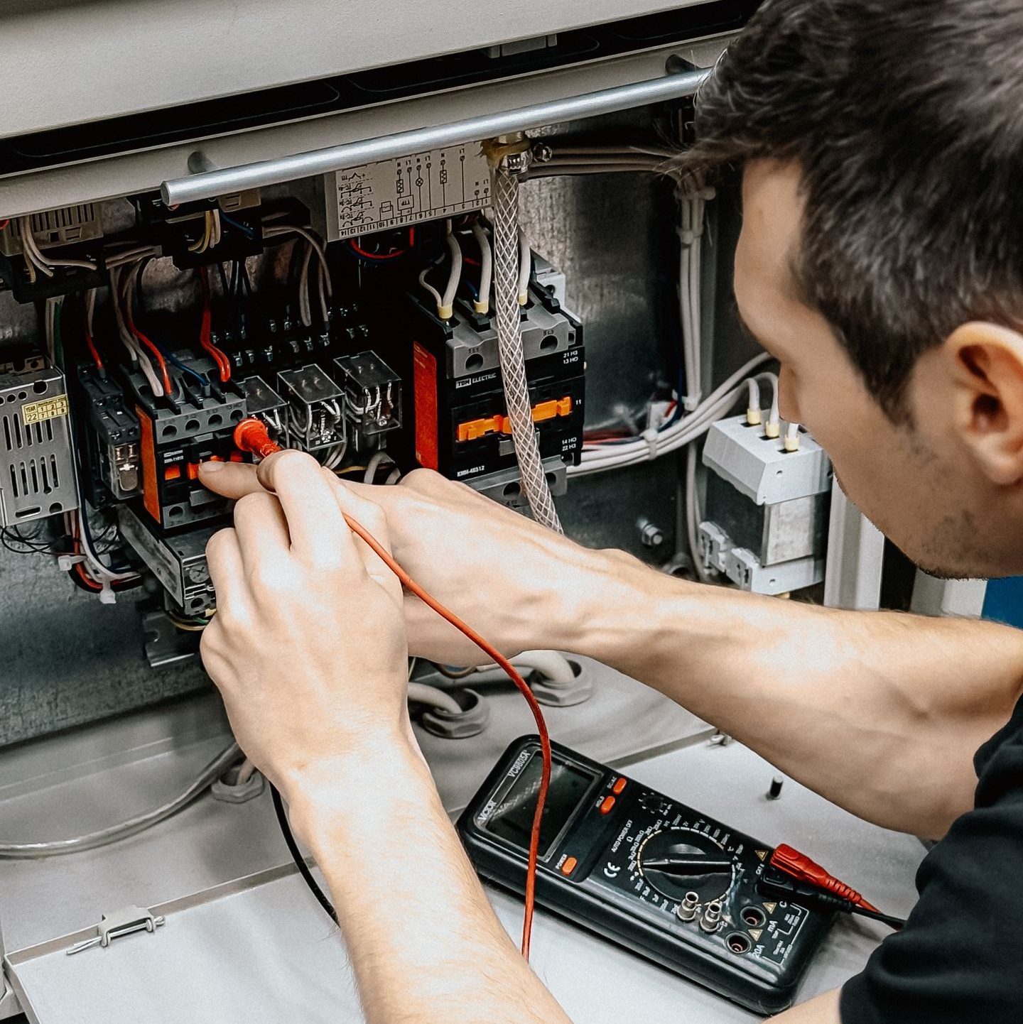 An electrician uses a multimeter to test and diagnose connections in an open electrical panel.